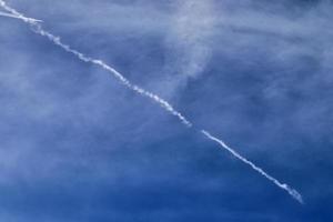 Aircraft condensation contrails in the blue sky inbetween some clouds photo