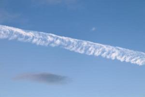 Aircraft condensation contrails in the blue sky inbetween some clouds photo