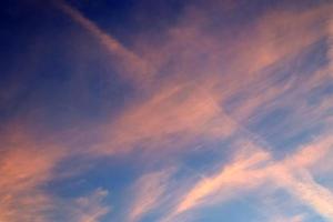 Aircraft condensation contrails in the blue sky inbetween some clouds photo