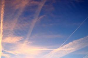 Aircraft condensation contrails in the blue sky inbetween some clouds photo