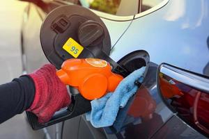 Gasoline filling nozzle 95 orange in the hand of the employee to fill the black car with gas. Soft and selective focus. photo