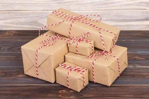 algunos paquetes de papel cajas de regalo de navidad envueltos con papel kraft y atados con hilo de panadero blanco rojo en una mesa de madera oscura. cajas de regalo de navidad foto