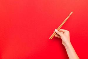 imagen recortada de la mano femenina sosteniendo palillos sobre fondo rojo. concepto de comida japonesa con espacio de copia foto