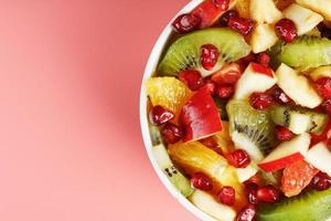 Bowl with fruit salad on a pink background. Juicy and ripe fruit slices. photo