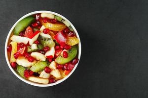 taza de ensalada de fruta fresca hecha de frutas jugosas sobre un fondo negro. foto