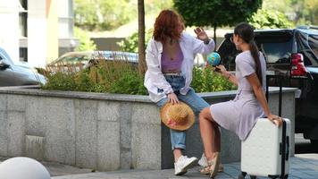 Two women with luggage outside talk and explore video