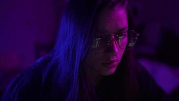 Young woman in a dark purple room with laptop screen reflection on eyeglasses video