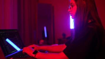 Young woman in a dark purple room uses a laptop video