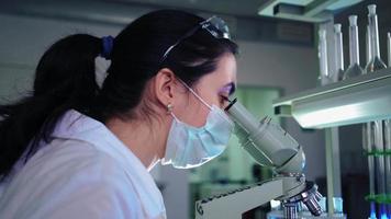vrouw microbioloog op zoek in microscoop in medisch wetenschap laboratorium. wetenschapper, werken met high Tech apparatuur. farmaceutisch geneesmiddel, biochemie, wetenschap concept. video