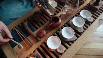 traditionelle Teezubereitung auf einem Brett für eine Teezeremonie bei Kerzenlicht mit sanftem Tageslicht. Mann gießt kochendes Wasser in eine Teekanne. Ansicht von oben. nicht erkennbarer Mensch. video