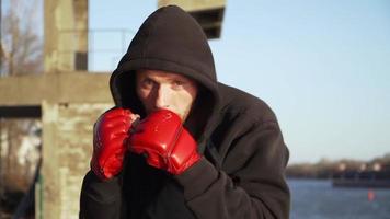 ein kerl mit kaukasischem aussehen ein boxer in roten handschuhen macht eine kampfübung mit schatten zur kamera. Zeitlupe. Motivationsvideo. video