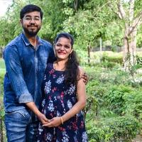 Indian couple posing for maternity baby shoot. The couple is posing in a lawn with green grass and the woman is falunting her baby bump in Lodhi Garden in New Delhi, India photo