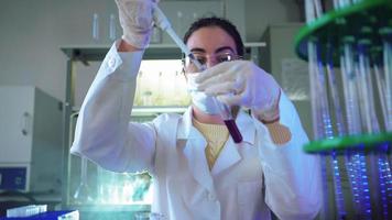 mujer científica en laboratorio haciendo experimentos químicos con líquido azul en tubos de ensayo. extracción de ADN y moléculas. desarrollo de vacunas. investigación, bioquímica, concepto de medicina farmacéutica. video