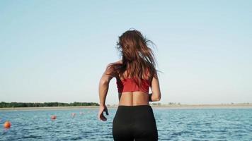 een jong atletisch Kaukasisch meisje loopt langs de pantone naar de meer. spelen sport. gezond levensstijl. langzaam beweging. video