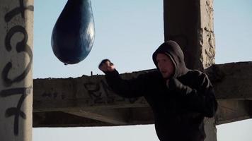 Boxer training outdoors in an abandoned building. The guy in the hood hits the pear. Theme of sport and healthy lifestyle. Martial arts. Slow motion. Static frame. video