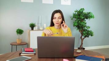 signora alunno e apprendimento utilizzando il computer portatile webcam Chiacchierare fa Appunti e Lavorando a partire dal casa. giovane bella ragazza nel un' giallo maglione impara in linea con un' insegnante di conferenza chiamata. distanza formazione scolastica concetto. video