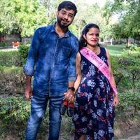 Indian couple posing for maternity baby shoot. The couple is posing in a lawn with green grass and the woman is falunting her baby bump in Lodhi Garden in New Delhi, India photo