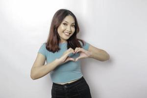 An attractive young Asian woman wearing a blue t-shirt feels happy and a romantic shapes heart gesture expresses tender feelings photo