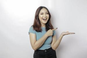 mujer asiática emocionada con una camiseta azul apuntando al espacio de la copia a su lado, aislada de fondo blanco foto