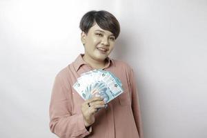 A happy young woman is wearing pink shirt and holding cash money in Indonesian rupiah isolated by white background photo