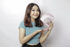 A happy young woman is wearing blue t-shirt and holding cash money in Indonesian rupiah isolated by white background photo