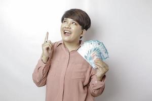 A happy young woman is wearing pink shirt and holding cash money in Indonesian rupiah isolated by white background photo