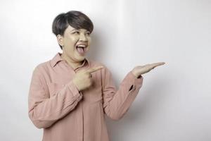 emocionada mujer asiática de pelo corto con un pantalones rosa apuntando al espacio de copia a su lado, aislada por un fondo blanco foto