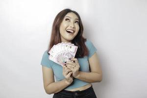 A happy young woman is wearing blue t-shirt and holding cash money in Indonesian rupiah isolated by white background photo