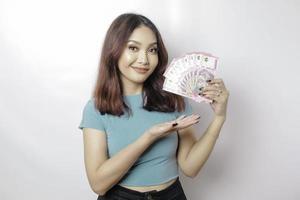 A happy young woman is wearing blue t-shirt and holding cash money in Indonesian rupiah isolated by white background photo