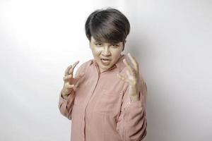 The angry and mad face of short-haired Asian woman in pink shirt on isolated blue background. photo