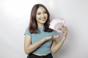 A happy young woman is wearing blue t-shirt and holding cash money in Indonesian rupiah isolated by white background photo