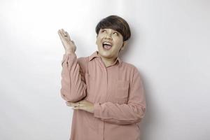 Excited Asian woman wearing pink shirt pointing at the copy space upside her, isolated by white background photo