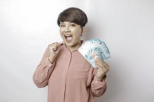 A happy young woman is wearing pink shirt and holding cash money in Indonesian rupiah isolated by white background photo