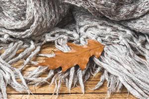 Crumpled grey knitted blanket with autumn oak leaf. Soft and warm fabric is crumpled into folds. Texture for background or illustrations photo