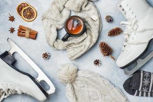 Winter vacation concept. Skates warm clothes, Cup of hot tea with fragrant spices on grey background. photo