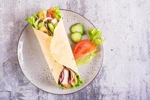 Mexican tortilla wraps with  vegetables and chicken on a plate on the table. Top view. Closeup photo