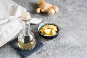 botella con suero de jengibre natural y jengibre picado en un bol sobre la mesa. cosméticos de cuidado natural. foto