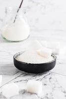 Granulated sugar and sugar cubes in a bowl and sugar in a jar on the table. Vertical view photo