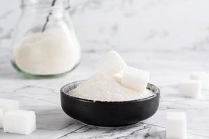 Granulated sugar and sugar cubes in a bowl and sugar in a jar on the table. photo