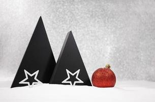 Black triangles of Christmas tree with white stars and red shiny ball on the snow. Defocus background. New Year. Copy space photo