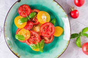 Fresh salad of yellow and red tomatoes with basil leaves on a plate on the table. Top view. Closeup photo