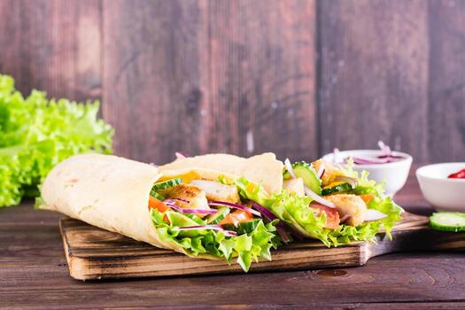envolturas de tortilla mexicana con pollo y verduras en un tablero sobre la mesa foto