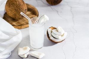 Coconut milk in a glass and pieces of tropical fruit on the table. Natural plant alternative photo