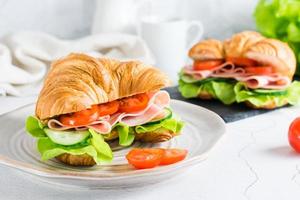 Sándwich de croissant fresco con jamón, verduras y lechuga en un plato. comida rápida casera. foto