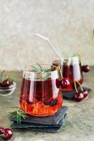 Cocktail with cherry, rosemary and ice in glasses on the table. Homemade mocktails. Vertical view photo