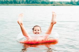 Cheerful girl sits in an inflatable ring with sticking legs in the river. Local tourism photo