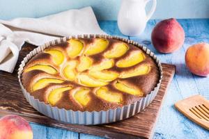 Ready fresh peach pie in a baking dish on the table. Homemade dessert photo