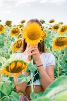 The girl covers her face with a sunflower in a field in the sun. Freedom and local tourism photo