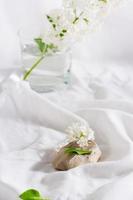 ramas de lila blanca sobre una piedra y en un vaso sobre un fondo de tela blanca. foto