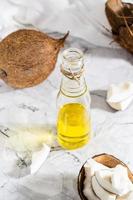 Fresh vegetable coconut oil in a bottle and pieces of coconut on the table. Vertical and above view photo